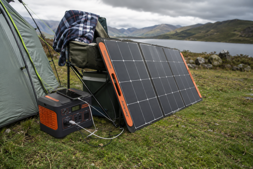 Foldable solar panel hanging from tent guy rope angled toward sky using carabiner loops while charging devices at UK campsite